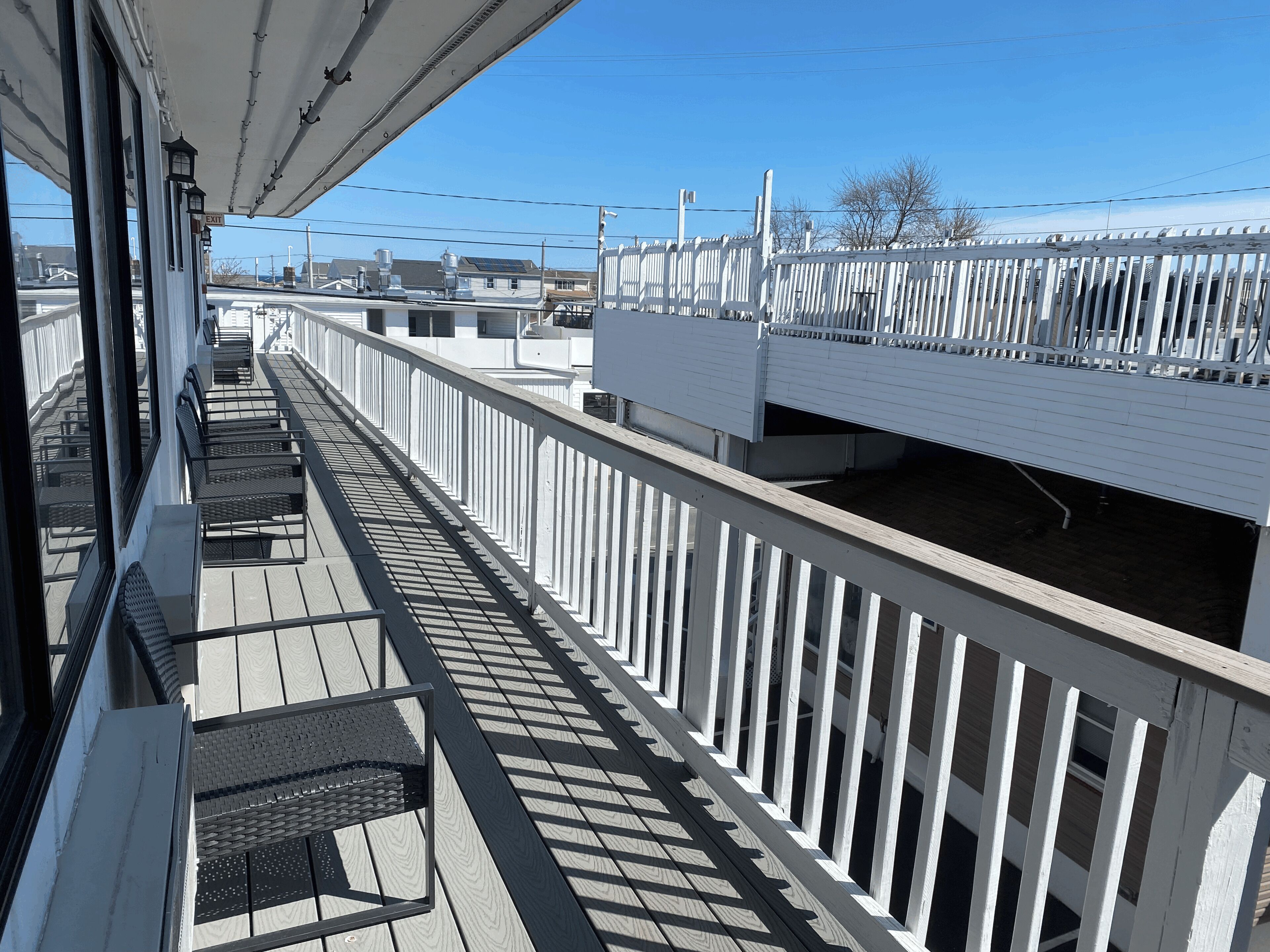 A wooden deck with white railings, a bench, and a view of buildings in the background.