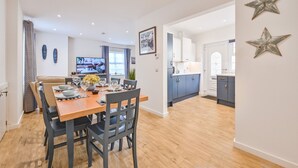 A modern kitchen with blue cabinets, a wooden dining table set for six, and a television in the background.