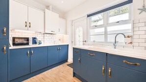 A modern kitchen with blue cabinets, a white countertop, and a window with a view of trees.
