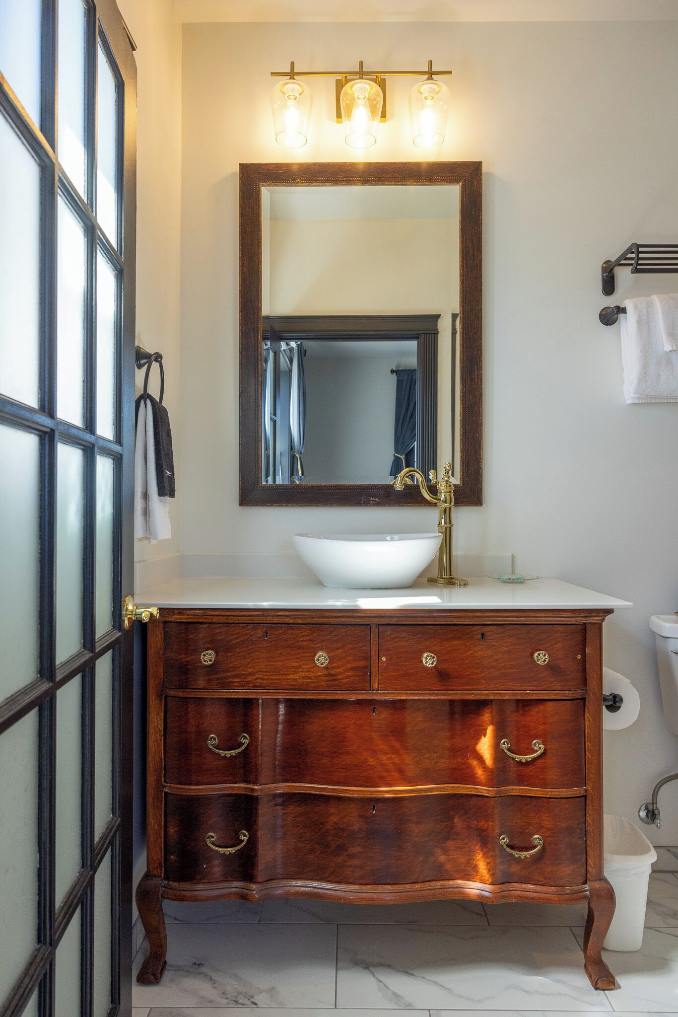 Un baño con tocador de madera, lavabo blanco y un espejo grande.