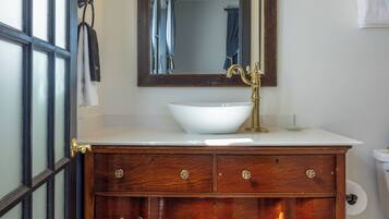 Un baño con tocador de madera, lavabo blanco y un espejo grande.