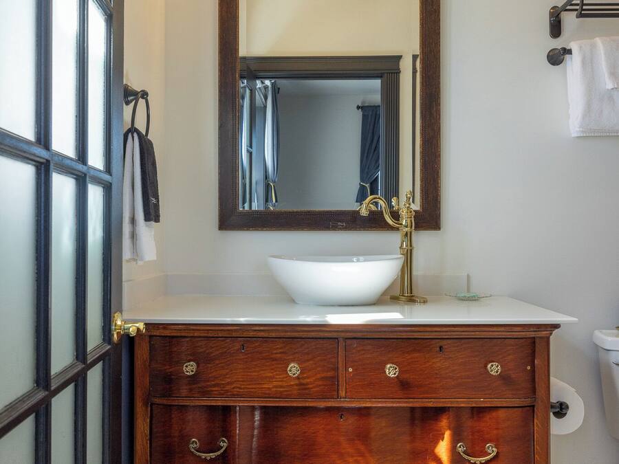 Un baño con tocador de madera, lavabo blanco y un espejo grande.