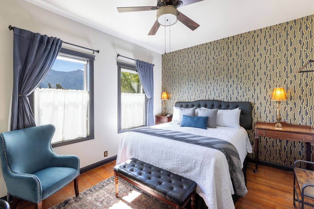 A bedroom with a large bed, a chair, a desk, and a ceiling fan.