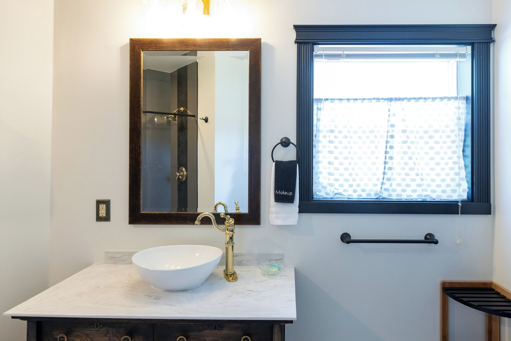 Une salle de bain avec un lavabo blanc, un miroir, un porte-serviettes et une fenêtre avec un rideau.