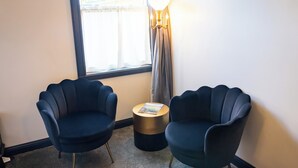 A room with two dark blue armchairs, a small round table with a book, a lamp, and a window with curtains. - Hotel Stevenson (Stevenson)