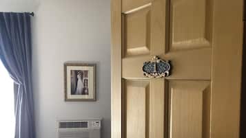 Una habitación con puerta de madera, un cuadro enmarcado en la pared, una ventana con cortinas y un radiador.