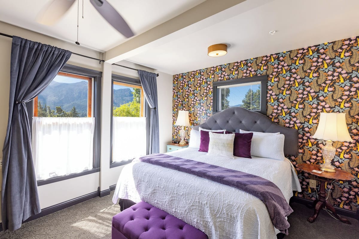 A bedroom with a large bed, a view of mountains, and patterned wallpaper.