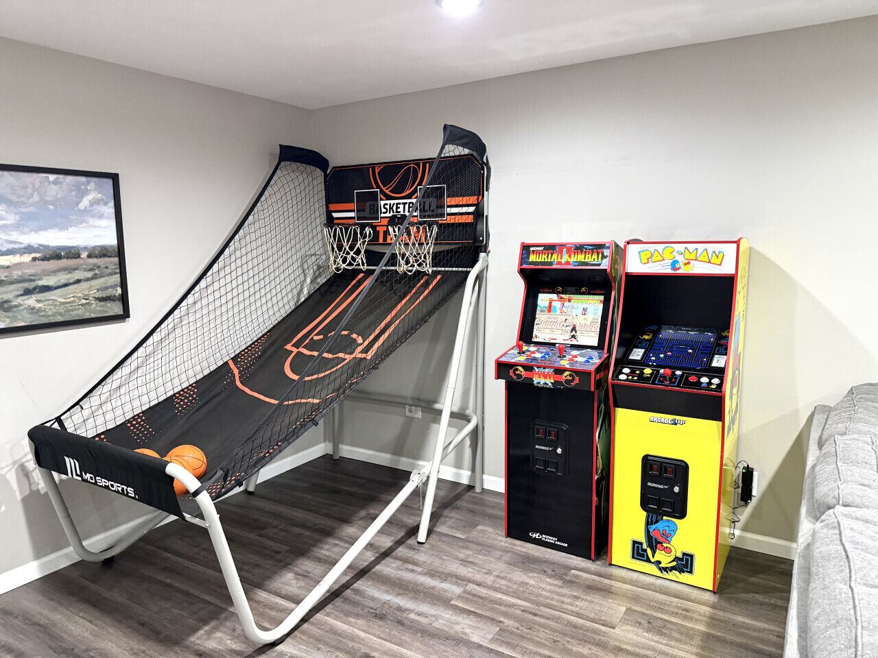 A room with a basketball goal, arcade machines, and a framed picture on the wall.
