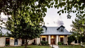 A two-story stone building with a metal roof, a central entrance, and a well-maintained lawn.