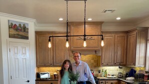 A kitchen with wooden cabinets, a central island with stools, and a hanging light fixture.