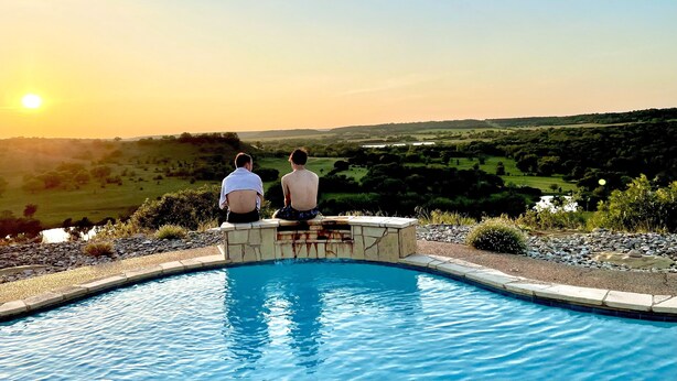Two people sitting by a pool with a sunset view.