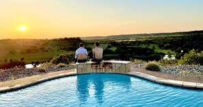 Deux personnes assises au bord d’une piscine, avec une vue sur le coucher de soleil.