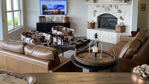 A cozy living room with leather sofas, a fireplace, and a television displaying a scenic image.