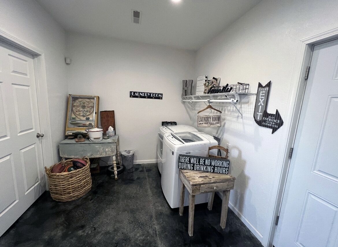 A laundry room with a sign indicating no working during drinking hours, a washing machine, a dryer, and a small table with a basket.