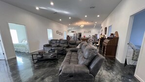 A spacious living room with a sectional sofa, a piano, and a view of the ocean through a door. - Private country getaway in the middle of nowhere! (Newtown)