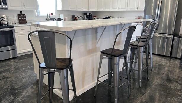 A modern kitchen with white cabinets, a large island with bar stools, stainless steel appliances, and a coffee machine. - Private country getaway in the middle of nowhere! (Newtown)