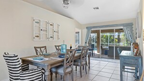 Un coin repas avec une table et des chaises en bois, un ventilateur de plafond et une vue sur l’extérieur grâce à une porte vitrée.