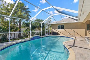 A swimming pool with a glass enclosure, surrounded by palm trees and a house. - Pet & family friendly villa w/bikes, ping pong table & fenced yard! Villa Avery - SWFL Rentals (Cape Coral)