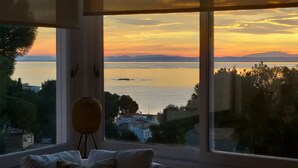 Una habitación con un amplio ventanal que da a una masa de agua y montañas distantes al atardecer.