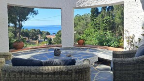 Un patio soleado con muebles de mimbre, plantas en macetas y vistas al mar.