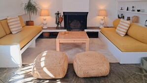Una sala de estar con chimenea, dos sofás, una mesa de centro y dos otomanas.