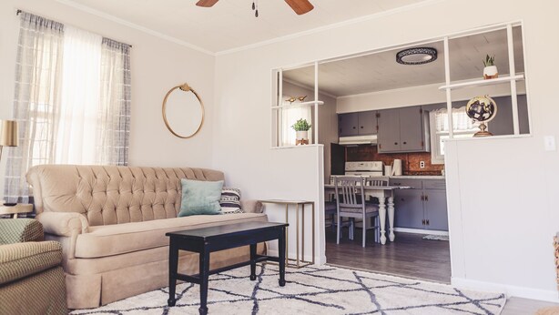 A living room with a beige sofa, a black coffee table, and a patterned rug. There is a ceiling fan, a window with sheer curtains, and a kitchen visible through an open doorway. - 2 Bedroom Home less than 2 miles to Jacks Fork River (Eminence)
