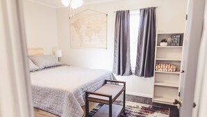 A bedroom with a bed, a small bench, a map on the wall, a shelf with decorative items, and a door. - 2 Bedroom Home less than 2 miles to Jacks Fork River (Eminence)