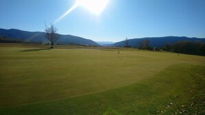 Ein Golfplatz mit blauem Himmel, fernen Bergen und einer Fahne, die das Abschlag-Areal markiert.