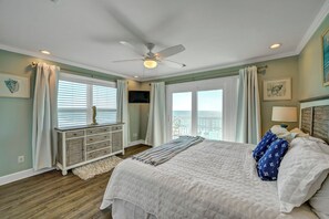 A bedroom with a bed, a ceiling fan, a TV, and a view of the ocean.