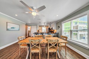 A dining area with a wooden table and chairs, a ceiling fan, and a view of the outside through large windows.