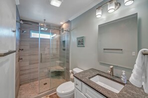 A modern bathroom with a glass-enclosed shower, a sink with a marble countertop, and a large mirror.