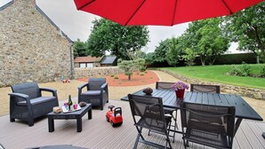 Une terrasse extérieure avec un mur en pierre, un parasol rouge et du mobilier d’extérieur.