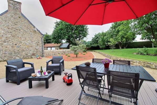 An outdoor patio with a stone wall, a red umbrella, and outdoor furniture.