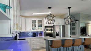 A modern kitchen with white cabinets, a central island with bar stools, stainless steel appliances, and pendant lighting. - Waterfront Renovated Luxury Home with pool and spa - 5 min walk to the beach (Indian Rocks Beach)
