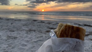 A piece of food on a paper wrapper on a beach with the sun setting in the background. - Waterfront Renovated Luxury Home with pool and spa - 5 min walk to the beach (Indian Rocks Beach)