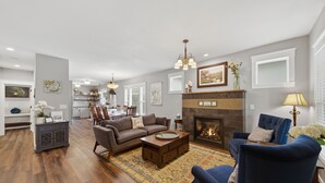 A spacious living room with a fireplace, a dining area, and a kitchen in the background. - Beautifully Renovated Historic Bungalow on Government Way (Coeur d'Alene)
