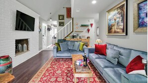 Un salon avec un canapé bleu, des coussins rouges, une table basse en bois et un tapis rouge à motifs.