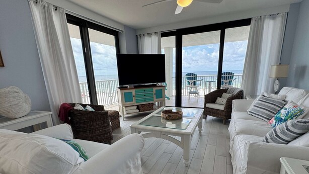 Un salon spacieux doté d’un grand téléviseur à écran plat, de canapés blancs, d’une table basse et d’un balcon offrant une vue sur la mer.