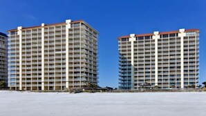 Deux immeubles de grande hauteur, dotés de nombreux balcons, qui font probablement partie d’un hôtel ou d’un complexe résidentiel, et qui sont situés sur une plage de sable fin, sous un ciel dégagé.