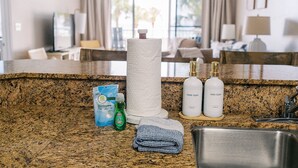 A granite countertop with a paper towel holder, dish soap bottles, a dishwashing liquid bottle, a hand soap bottle, and a towel. - Upscale Family-Friendly Beachfront Condo Conveniently Located (Gulf Shores)