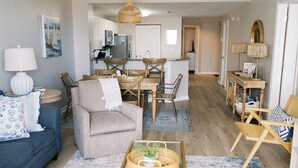 A living room with a sofa, armchair, coffee table, and a dining area with a table and chairs. - Upscale Family-Friendly Beachfront Condo Conveniently Located (Gulf Shores)