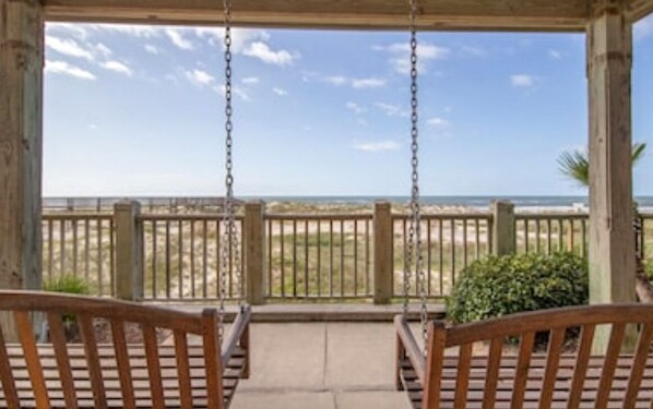 A wooden porch with two benches facing a beach view.