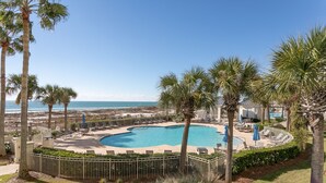 A pool area with lounge chairs and umbrellas, surrounded by palm trees and a view of the ocean. - Upscale Family-Friendly Beachfront Condo Conveniently Located (Gulf Shores)