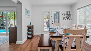 Un área de comedor con vista a la piscina, suelo de madera y un letrero que dice 'Life Better by the Pool'.
