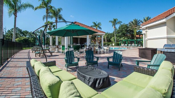 A patio area with green cushioned seating, a covered dining area, and a pool.
