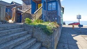 Een huis aan de kust met een houten gevel, een blauwe voordeur en een reeks stenen traptreden naar een veranda.