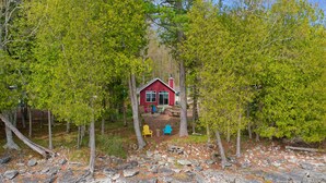 Eine rote Holzhütte, umgeben von Bäumen, mit einem Steinweg, der dorthin führt.