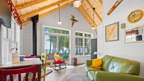 Ein gemütliches Zimmer mit Holzbalkendecke, einem grünen Ledersofa, einem Tisch mit Stühlen und Meerblick durch große Fenster.