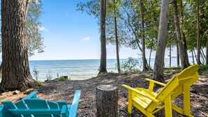 Ein Strandbild mit zwei Adirondack-Stühlen, einem blauen und einem gelben, in der Nähe eines Baumstumpfes platziert.