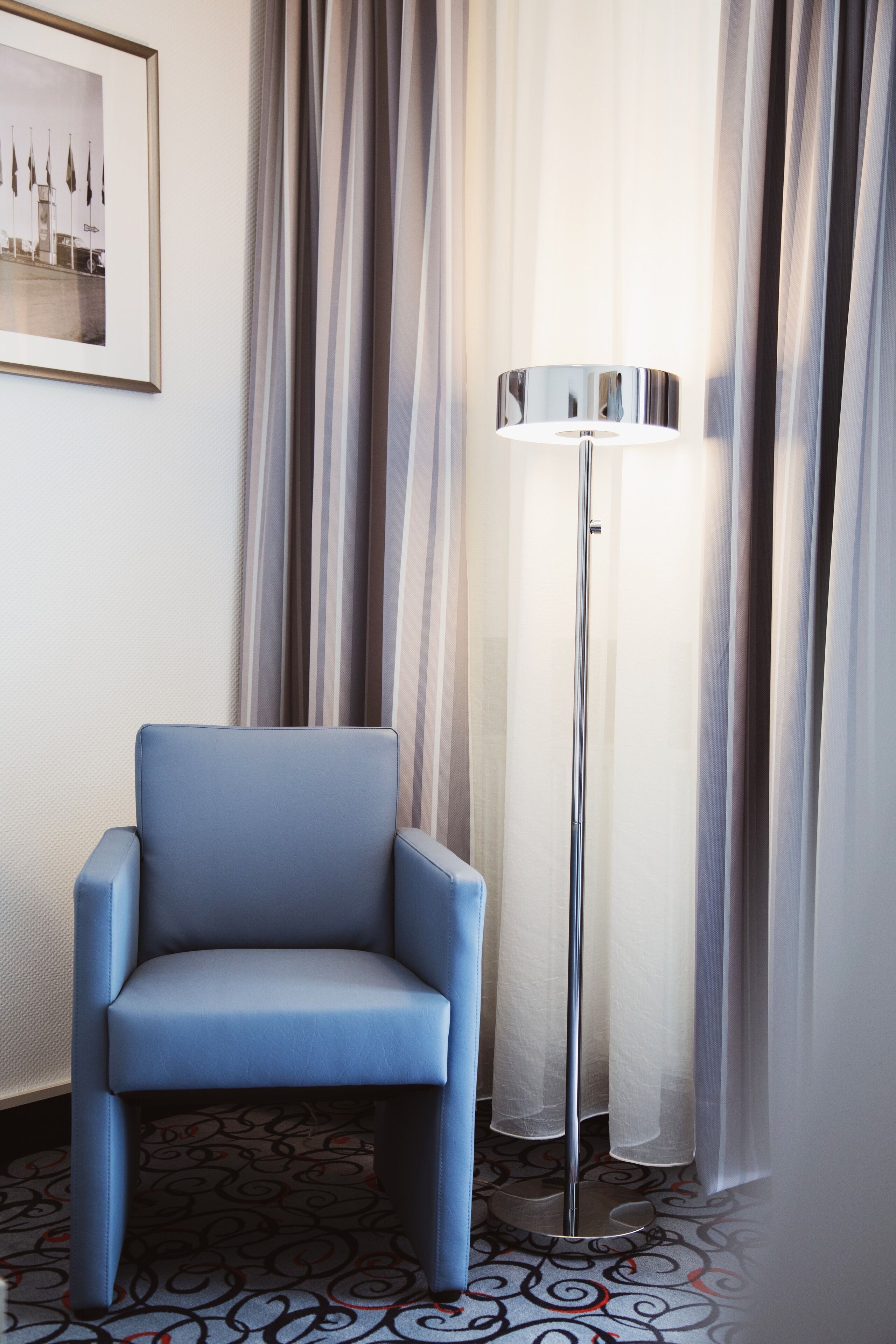 A room with a blue armchair, a floor lamp, and a patterned carpet.